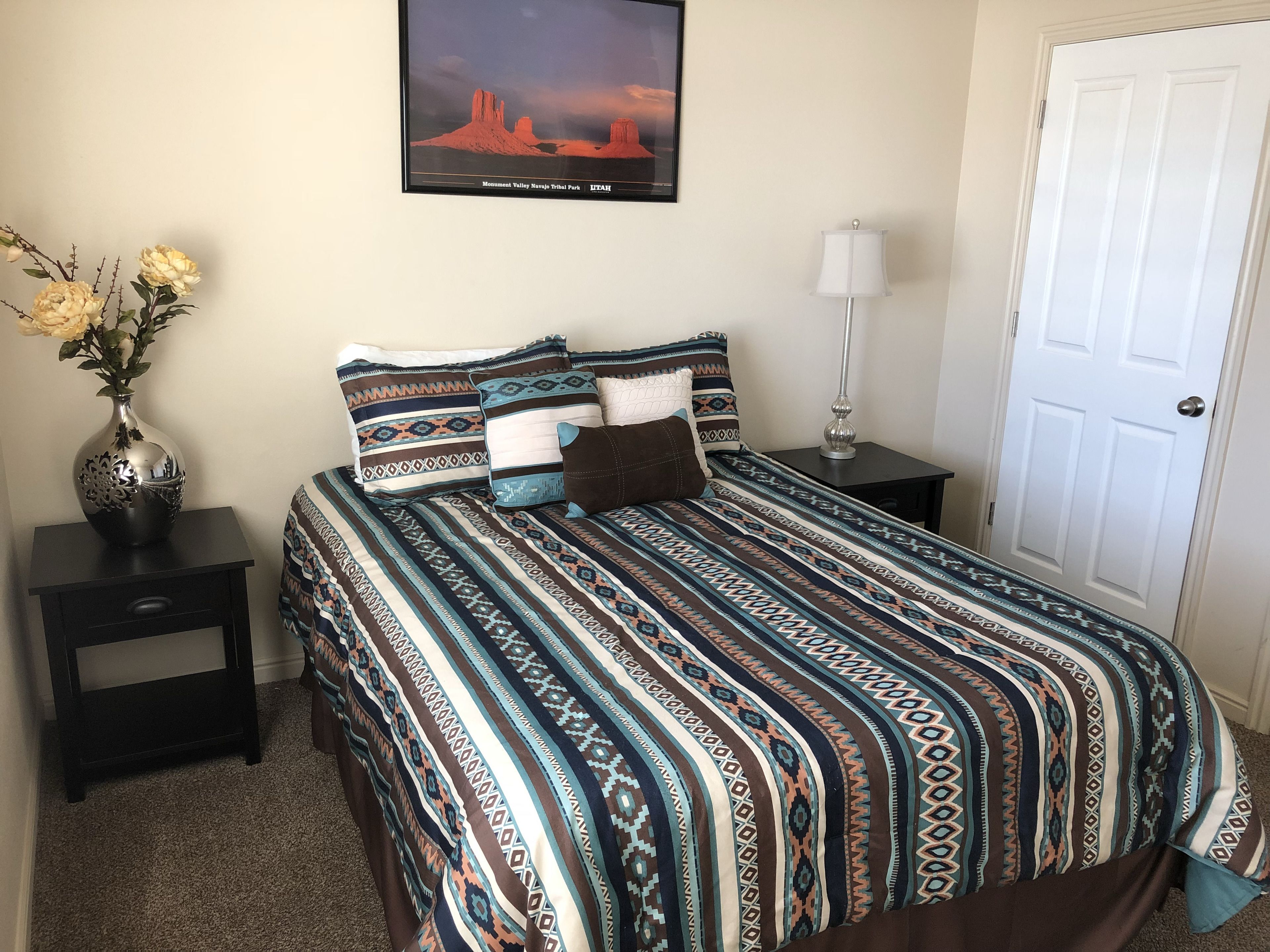 A bedroom with a bed, a nightstand, a lamp, a vase with flowers, and a framed picture on the wall.