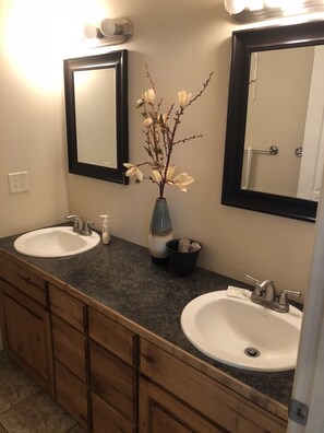 A bathroom with two sinks, a mirror, and a vase with flowers. - Cedar Canyon Condos (Blanding)