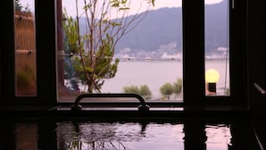A view through a window with a metal frame, a plant, and a body of water reflecting the sky. - Rako Hananoi Hotel (Suwa)