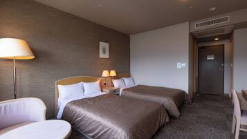 A hotel room with two beds, a desk, a chair, and a lamp.