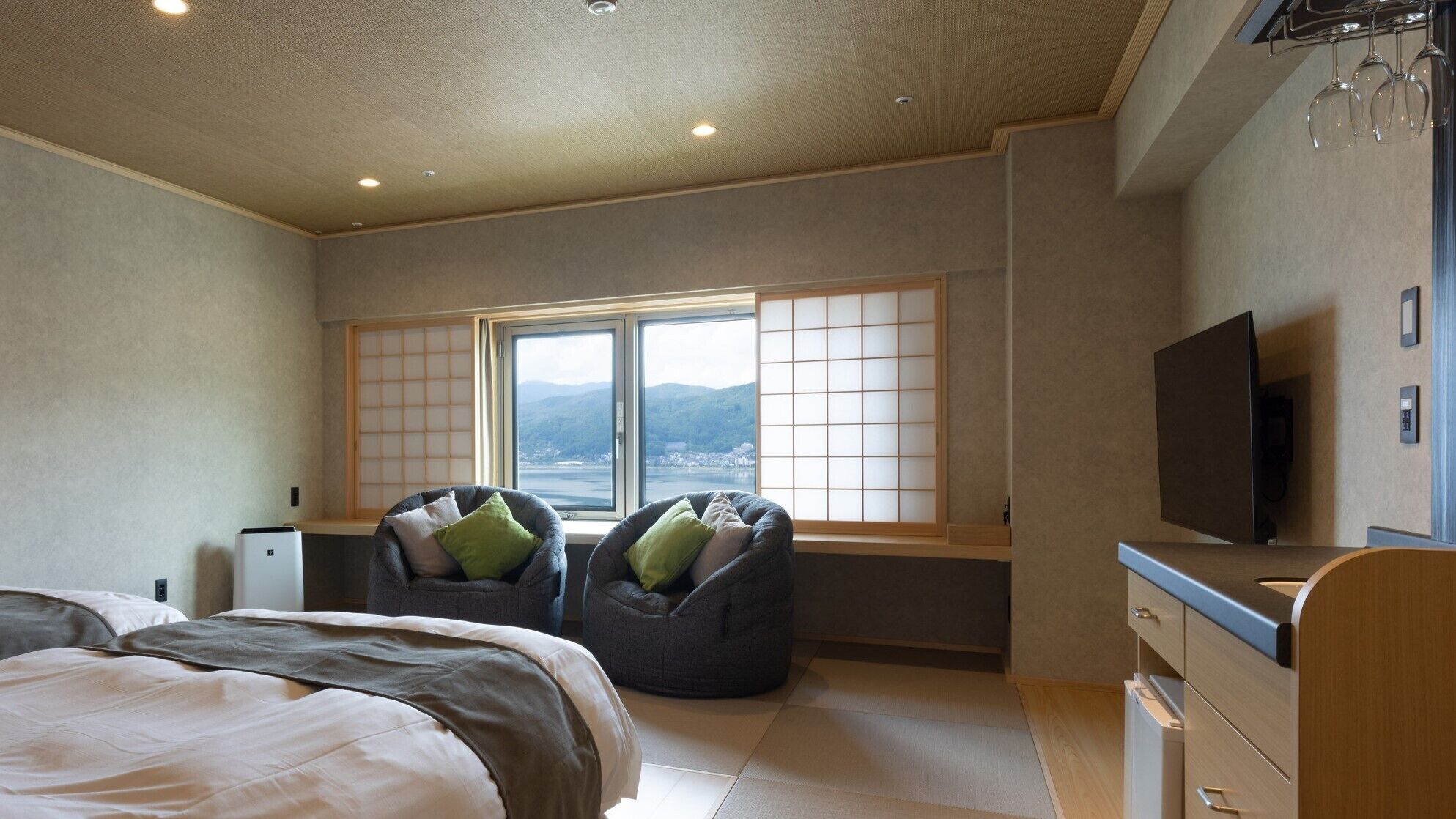 A bedroom with a bed, two bean bags, a TV, and a window with a view.