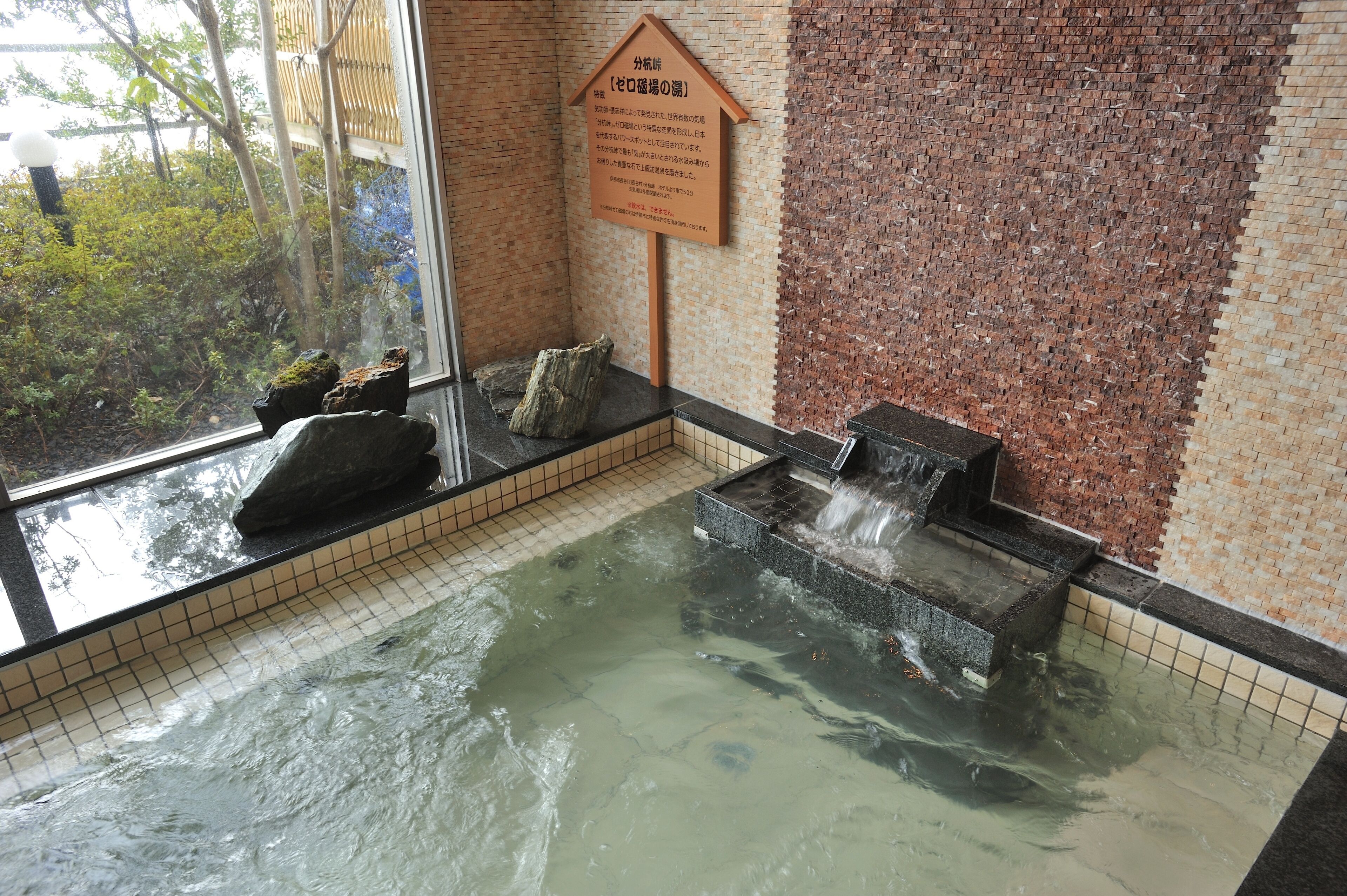 A hot spring area with a tiled floor, a wooden sign, and a stone basin.