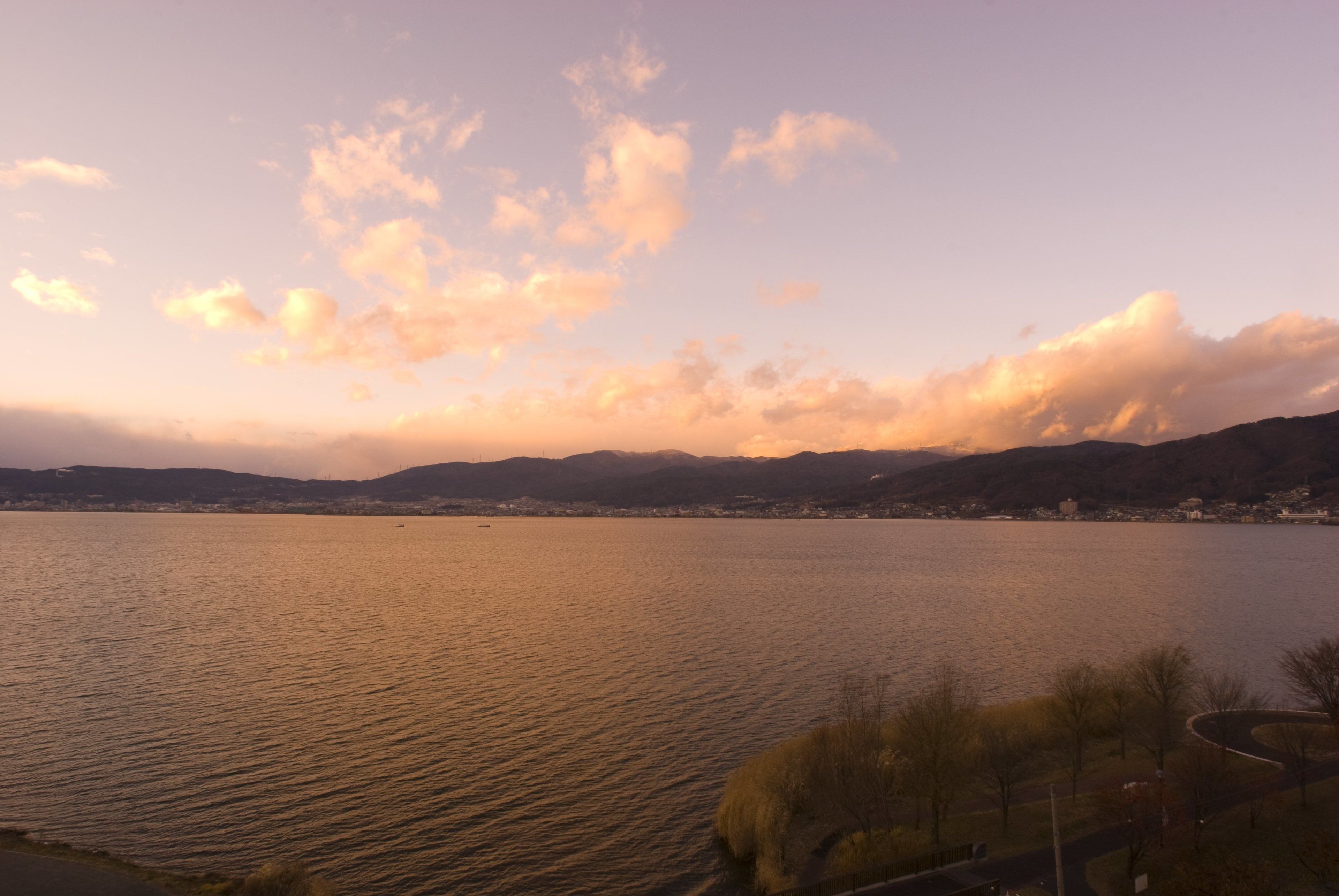 A calm lake with a distant shoreline, surrounded by hills and trees.