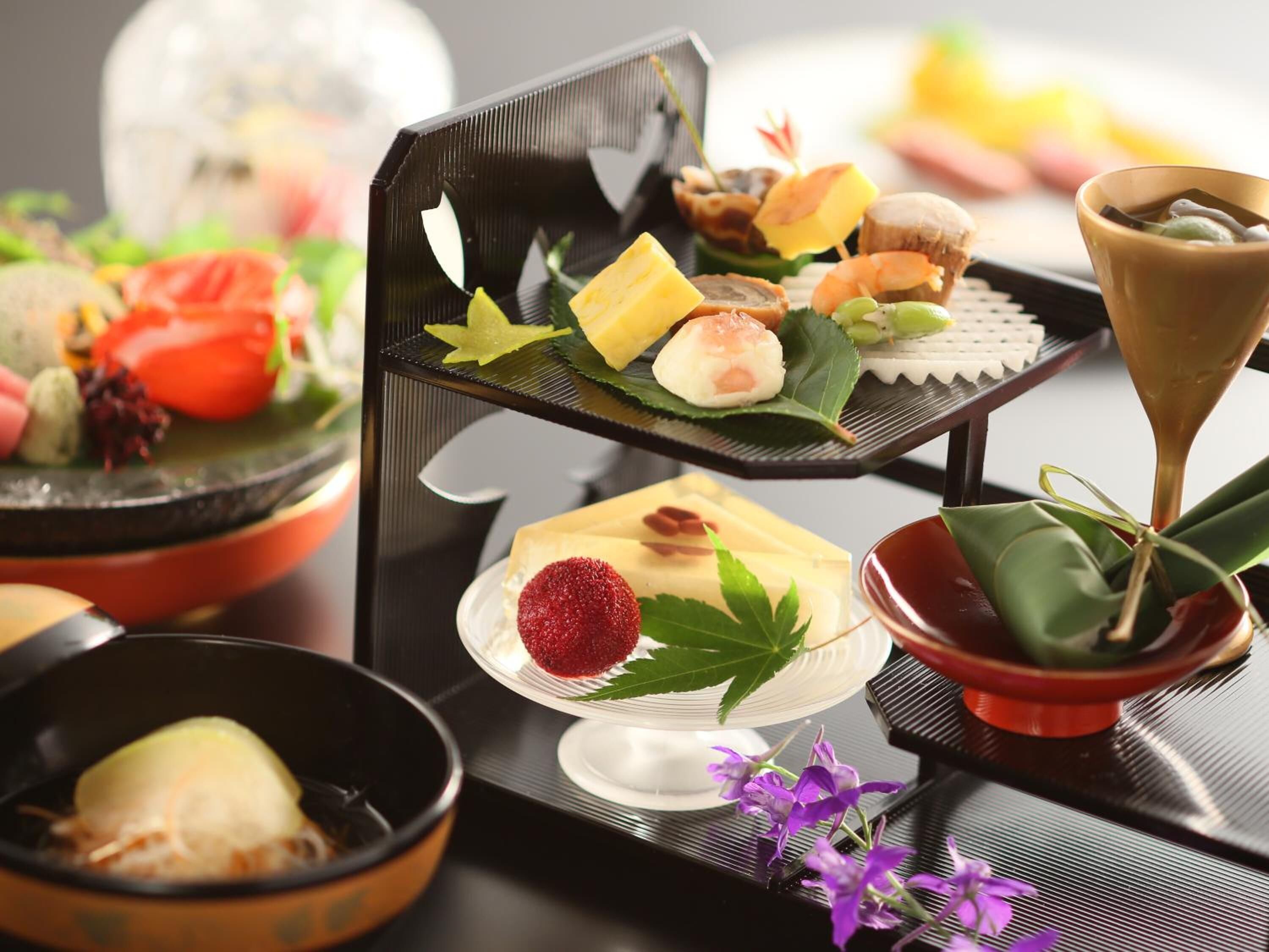 A multi-tiered serving tray with various food items, including sushi, a dessert, and a drink.