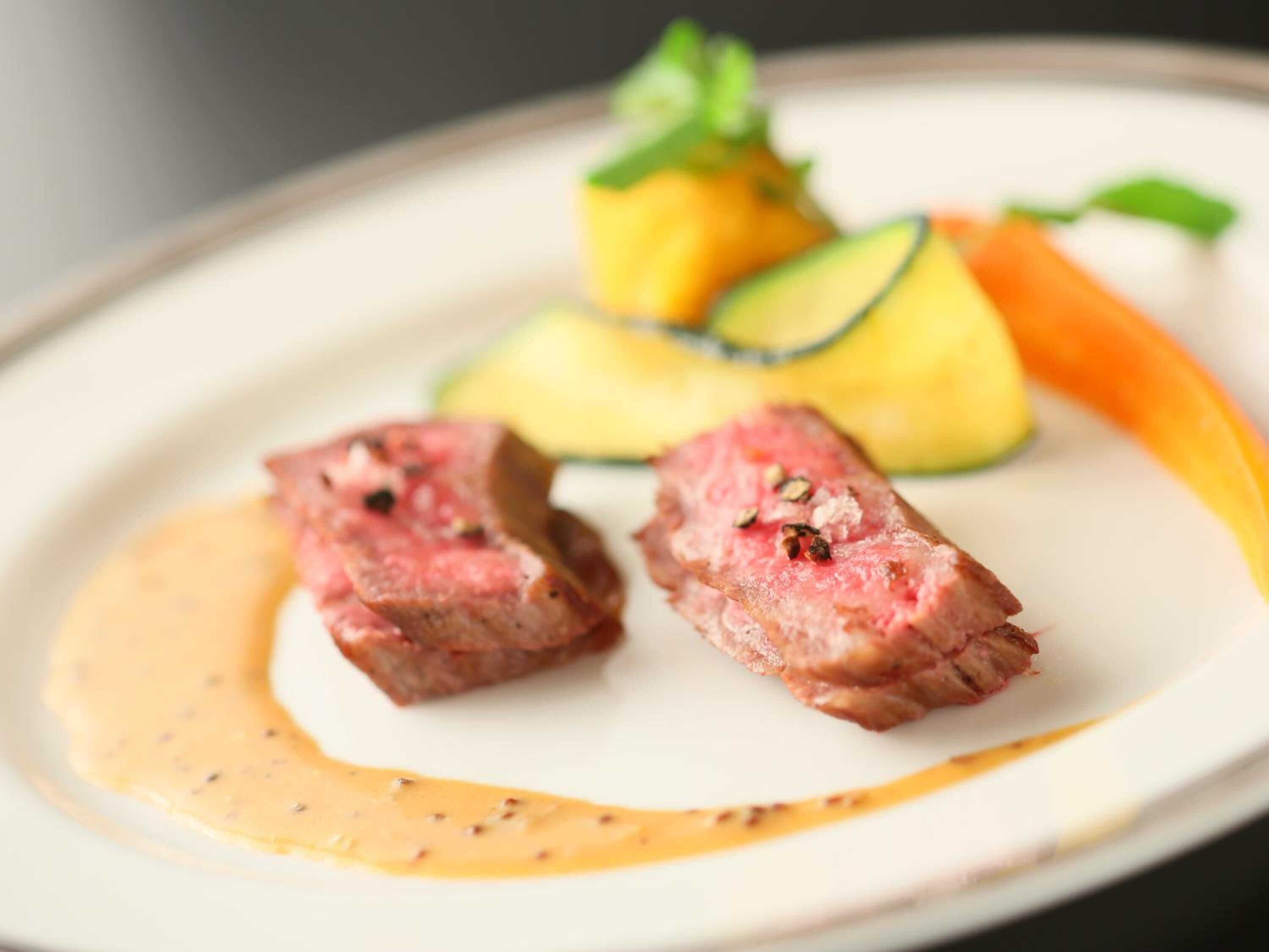 A plate with two pieces of steak, a slice of mango, and a carrot.