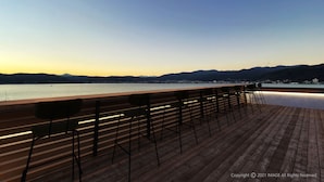 A wooden deck with bar stools overlooking a calm body of water and distant mountains. - Rako Hananoi Hotel (Suwa)