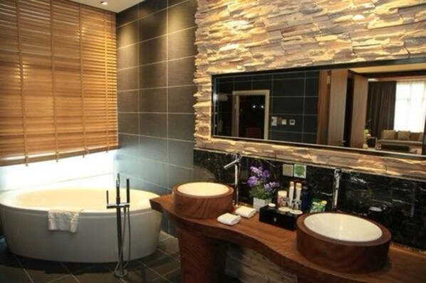 Un baño moderno con una bañera grande, dos lavamanos y una pared decorativa de piedra.