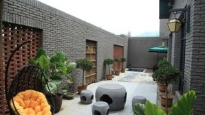 A courtyard with a brick wall, a hanging chair, potted plants, and stone planters. - Louguan Yinxiang Hotel Xi'an (Xi'an)