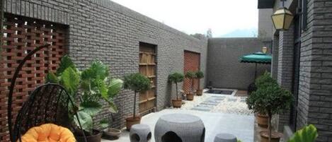 A courtyard with a brick wall, a hanging chair, potted plants, and stone planters.