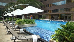 A swimming pool with lounge chairs and umbrellas, surrounded by greenery and a modern building in the background. - Yunkai Hotel (Guangzhou)