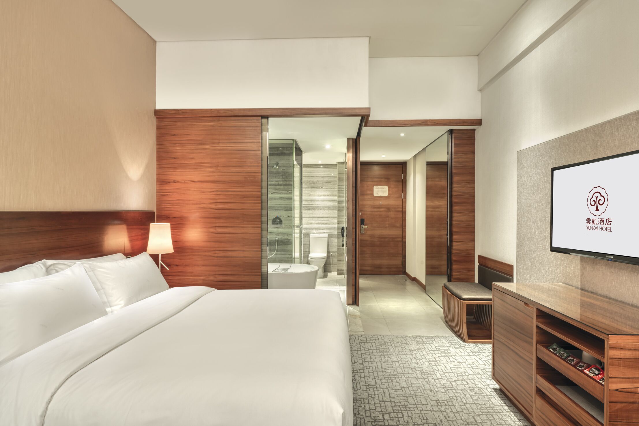 A modern hotel room with a large bed, a TV, a wooden wardrobe, and a glass-enclosed bathroom.
