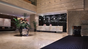 A modern hotel lobby with a reception desk, a large potted plant, and a marble floor. - Yunkai Hotel (Guangzhou)