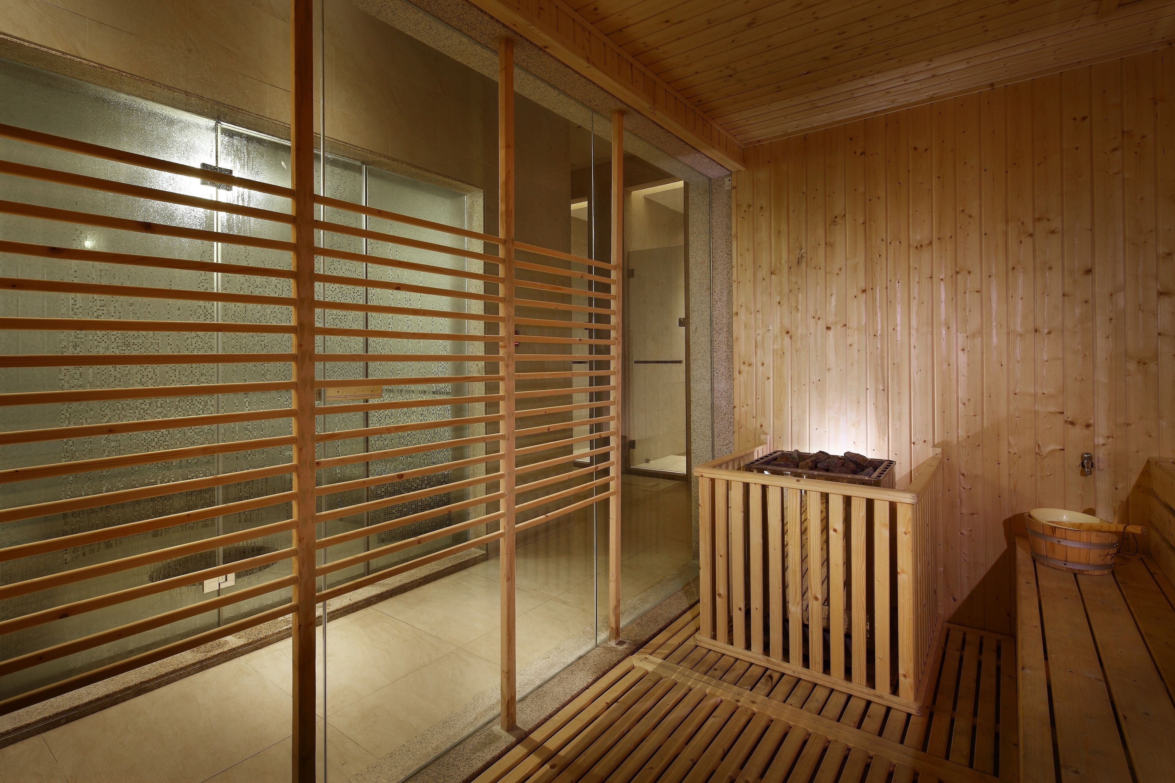 A wooden sauna room with a glass partition, a wooden bench, and a small sink.