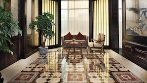 A lobby with a patterned floor, a sofa, a chair, and a large painting on the wall. - Yunkai Hotel (Guangzhou)