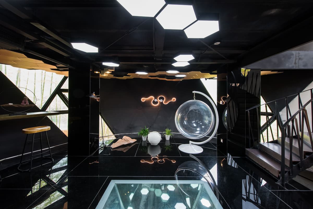 Un intérieur moderne avec une table en verre, des luminaires au plafond aux formes géométriques et un escalier.