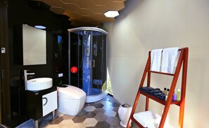 Un baño moderno con ducha envuelta en vidrio, un lavamanos blanco y un estante de madera con artículos de tocador.