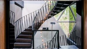 A modern staircase with a glass railing and metal balusters, leading to a landing with a view of greenery outside. - Planet Zero Retreat (Huzhou)