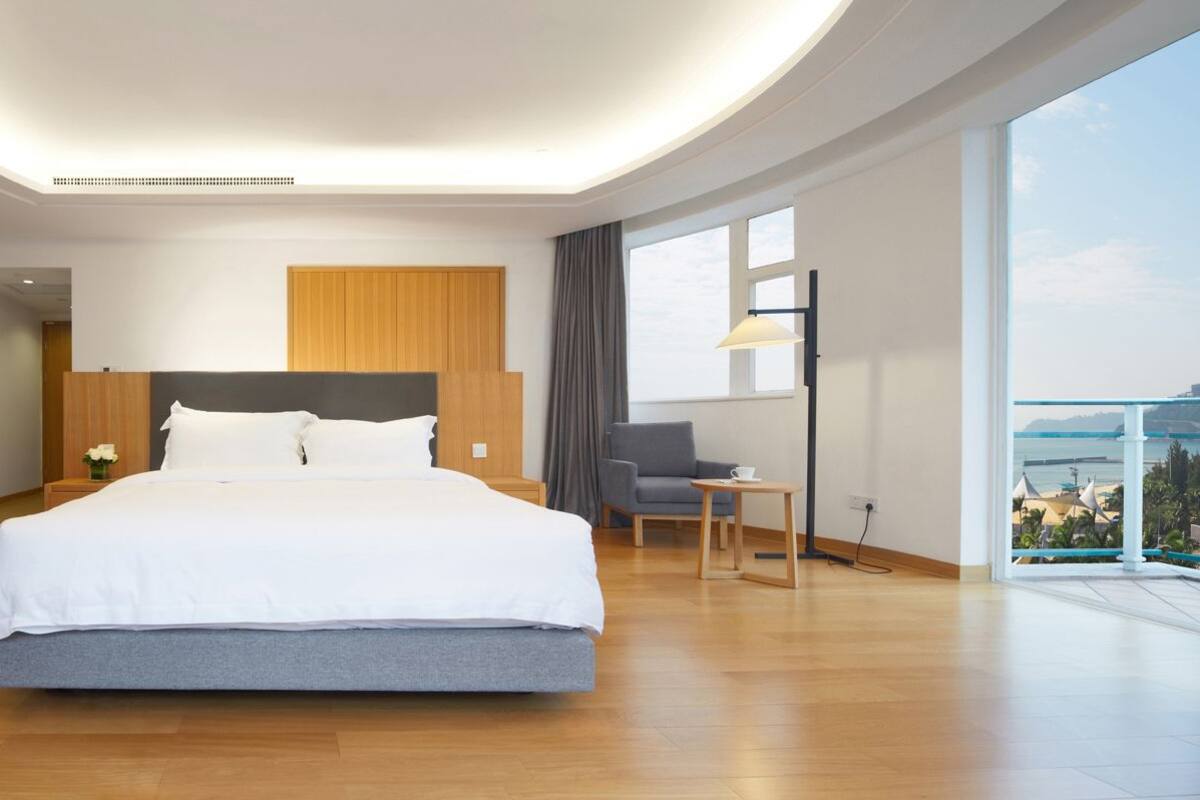 A modern hotel room with a large bed, a wooden headboard, a view of the sea, and a balcony.