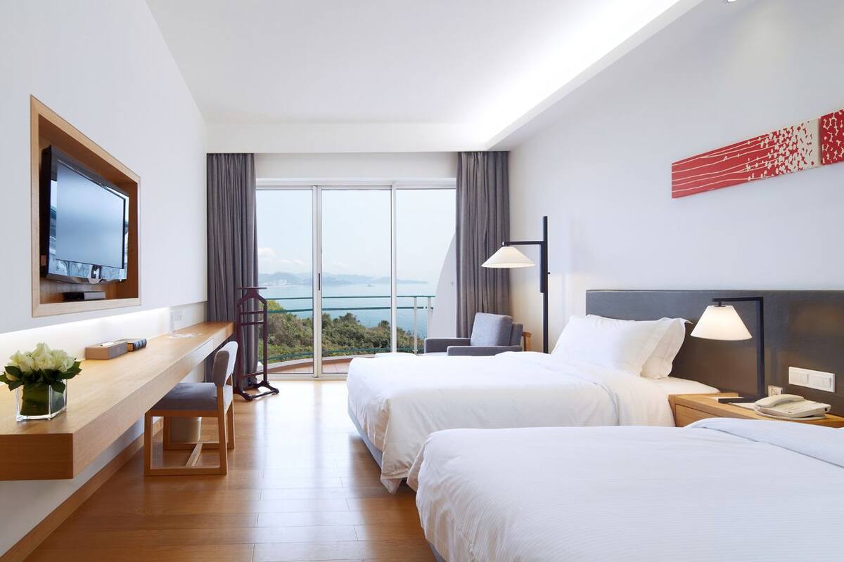 A hotel room with two beds, a desk, a TV, and a view of the outdoors.