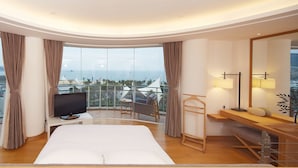 Een moderne hotelkamer met een groot bed, een televisie en een balkon met uitzicht op de stad en de zee.