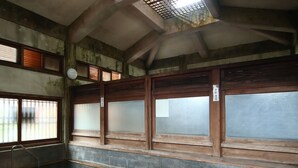 A traditional Japanese onsen with wooden sliding doors, a stone floor, and a small wooden bench. - Maruka Ryokan (Yamanouchi)