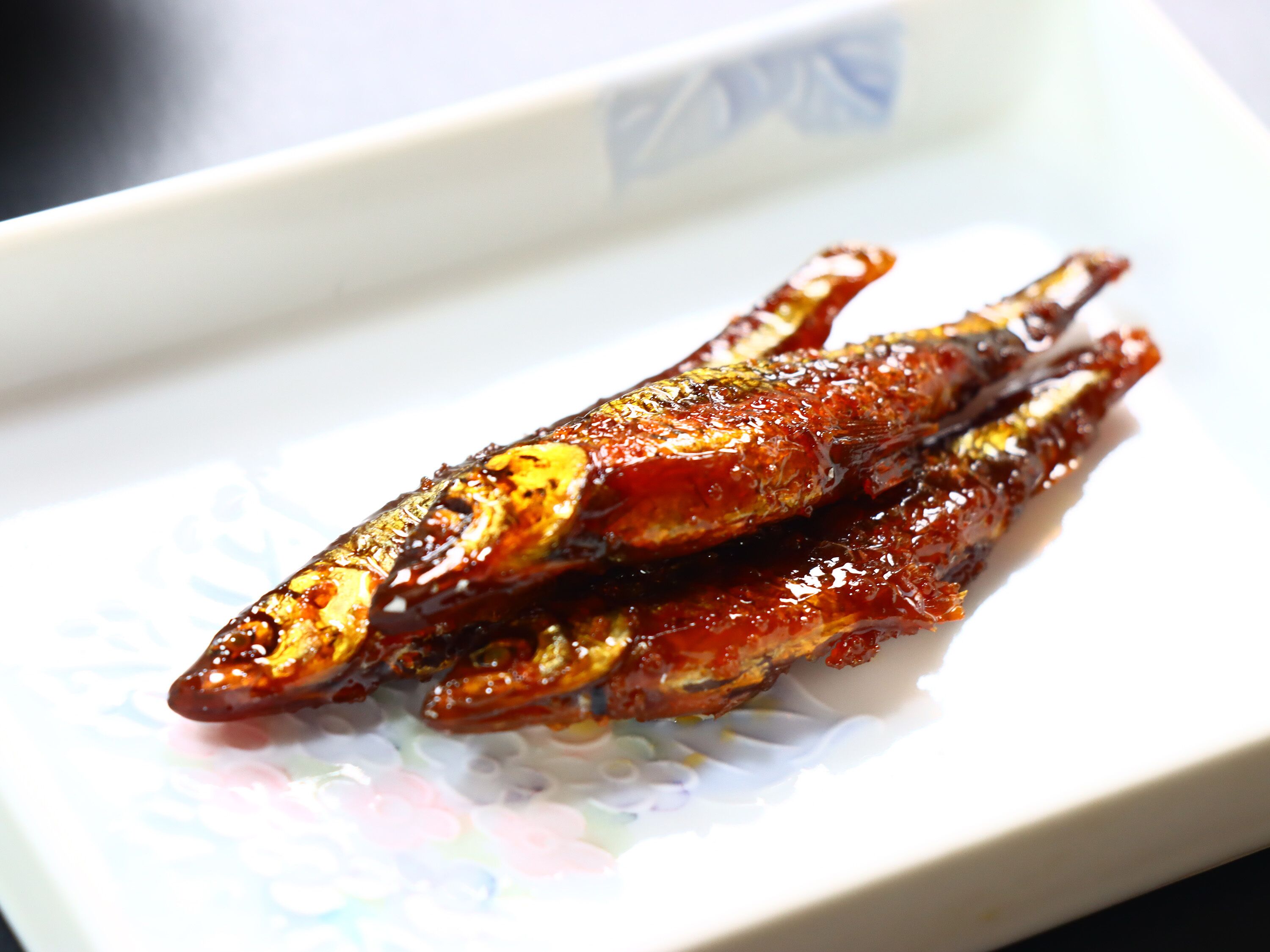 A plate with grilled fish, possibly marinated, on a patterned plate.