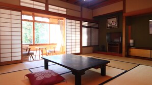 A tatami mat room with a low table, cushions, sliding doors, and a television. - Maruka Ryokan (Yamanouchi)