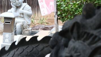 Una estàtua de Buda de pedra en un jardí, amb una tanca de fusta i vegetació al fons.