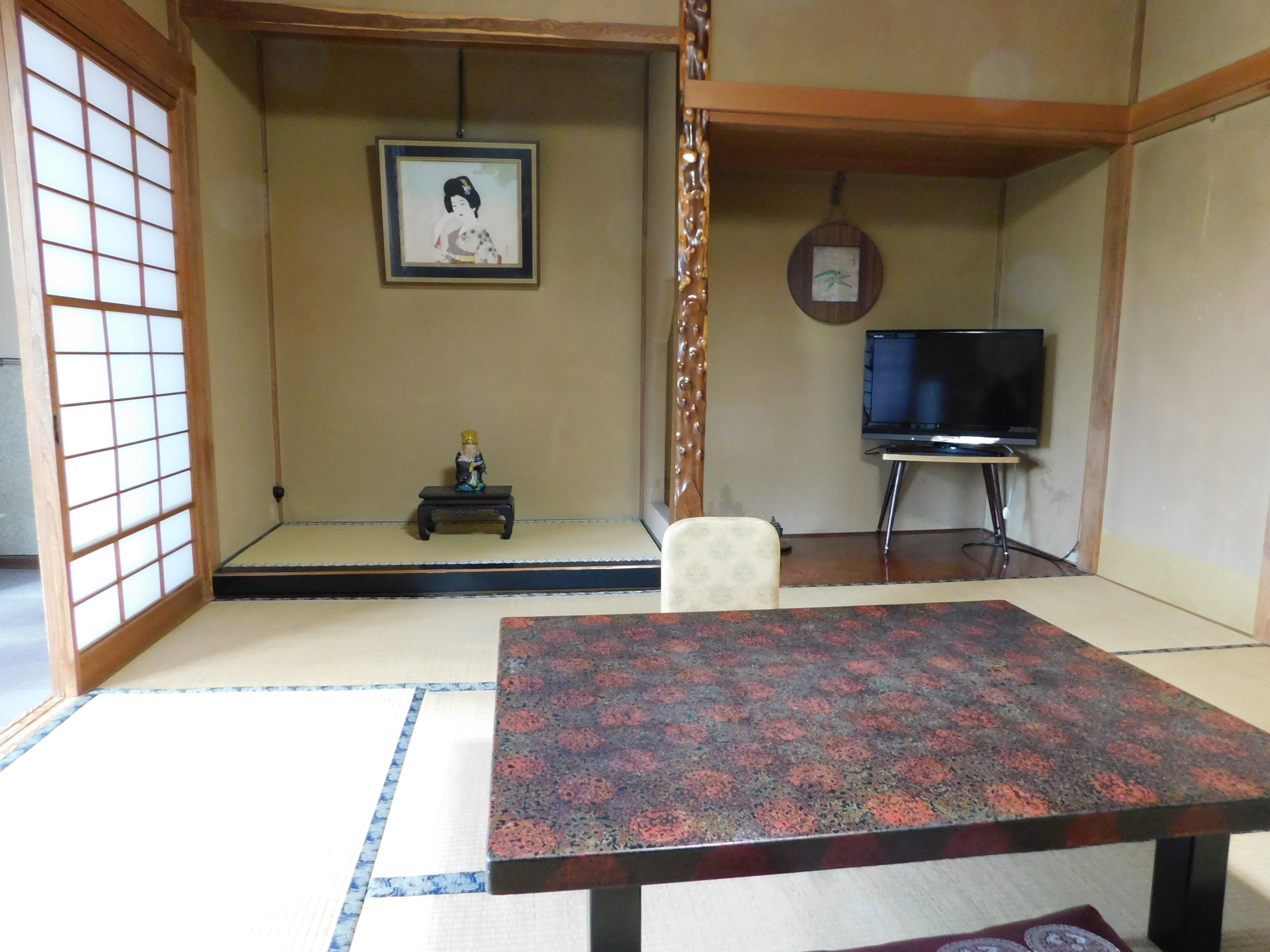 Um quarto japonês tradicional com tatames, uma mesa baixa, uma televisão e um quadro na parede.