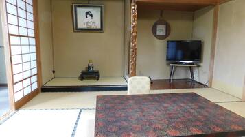 Um quarto japonês tradicional com tatames, uma mesa baixa, uma televisão e um quadro na parede.