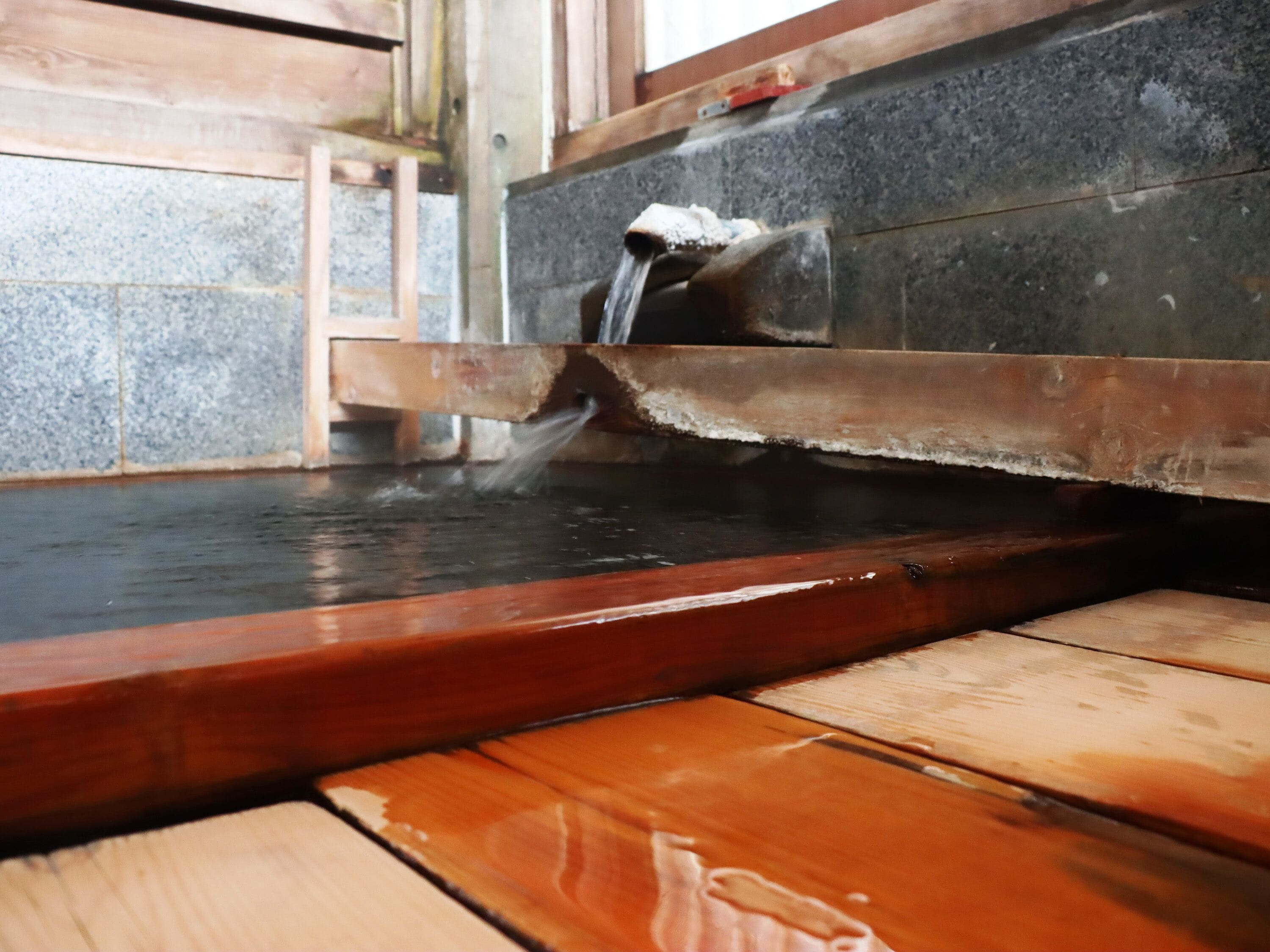 Un banco de madera con una pared de piedra y una pequeña fuente de agua.