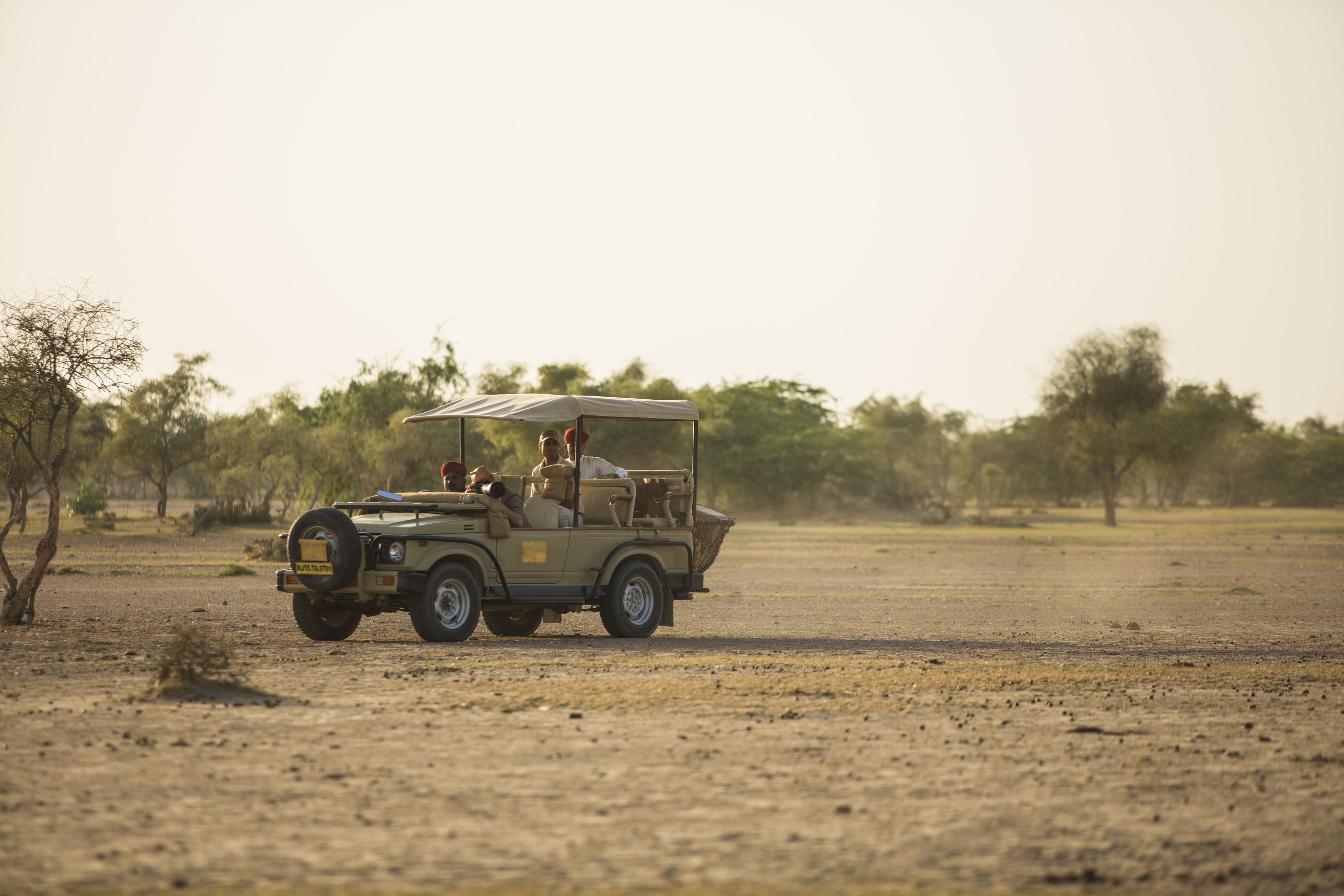 A safari vehicle with passengers and a guide, driving on a dirt road in a savannah landscape.