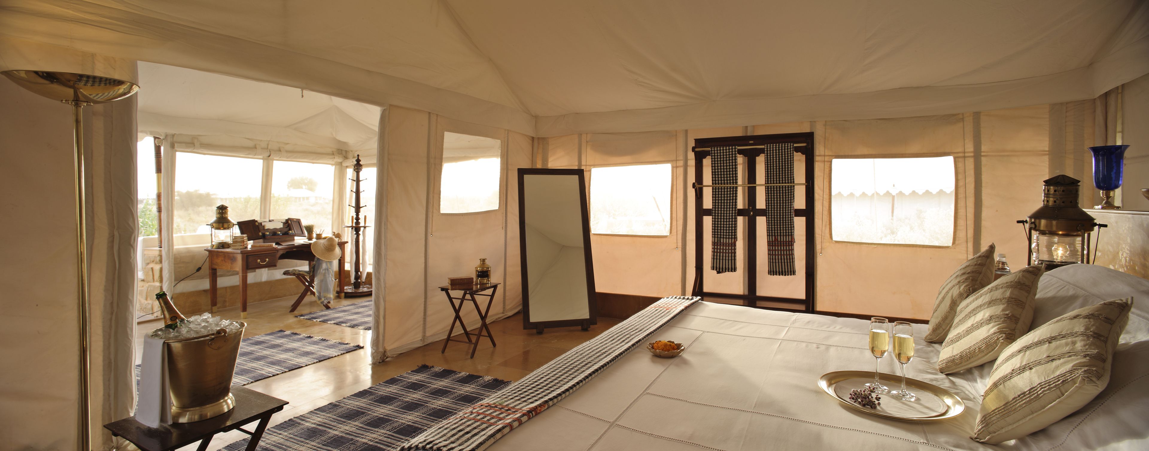 A tented room with a bed, a table with drinks, a mirror, and a view of the outside.