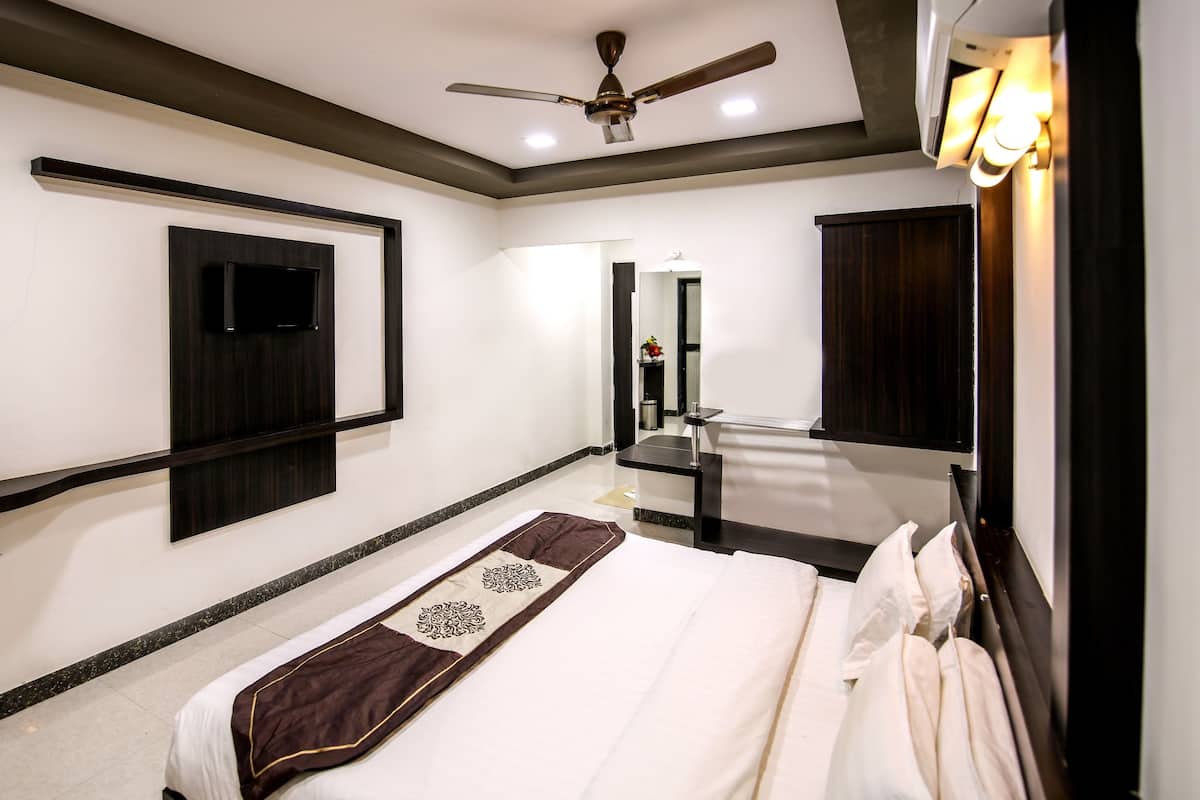 A hotel room with a bed, a ceiling fan, a TV mounted on the wall, a mirror, and a sink.