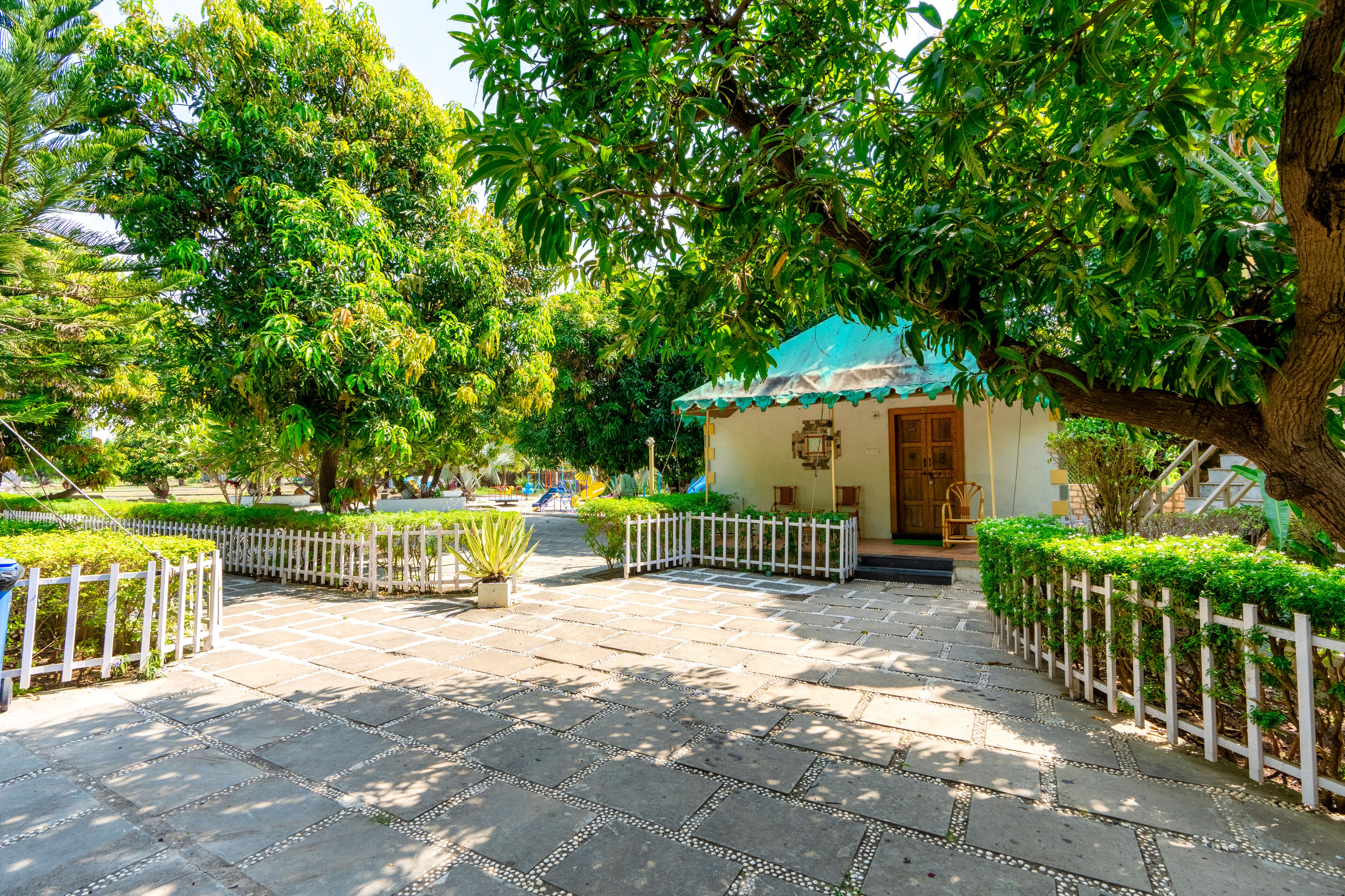 A courtyard with a small building, white picket fence, and lush greenery.