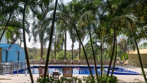 Ein Swimmingpool mit blau gefliestem Innenraum, umgeben von Palmen und einem blauen Gebäude.