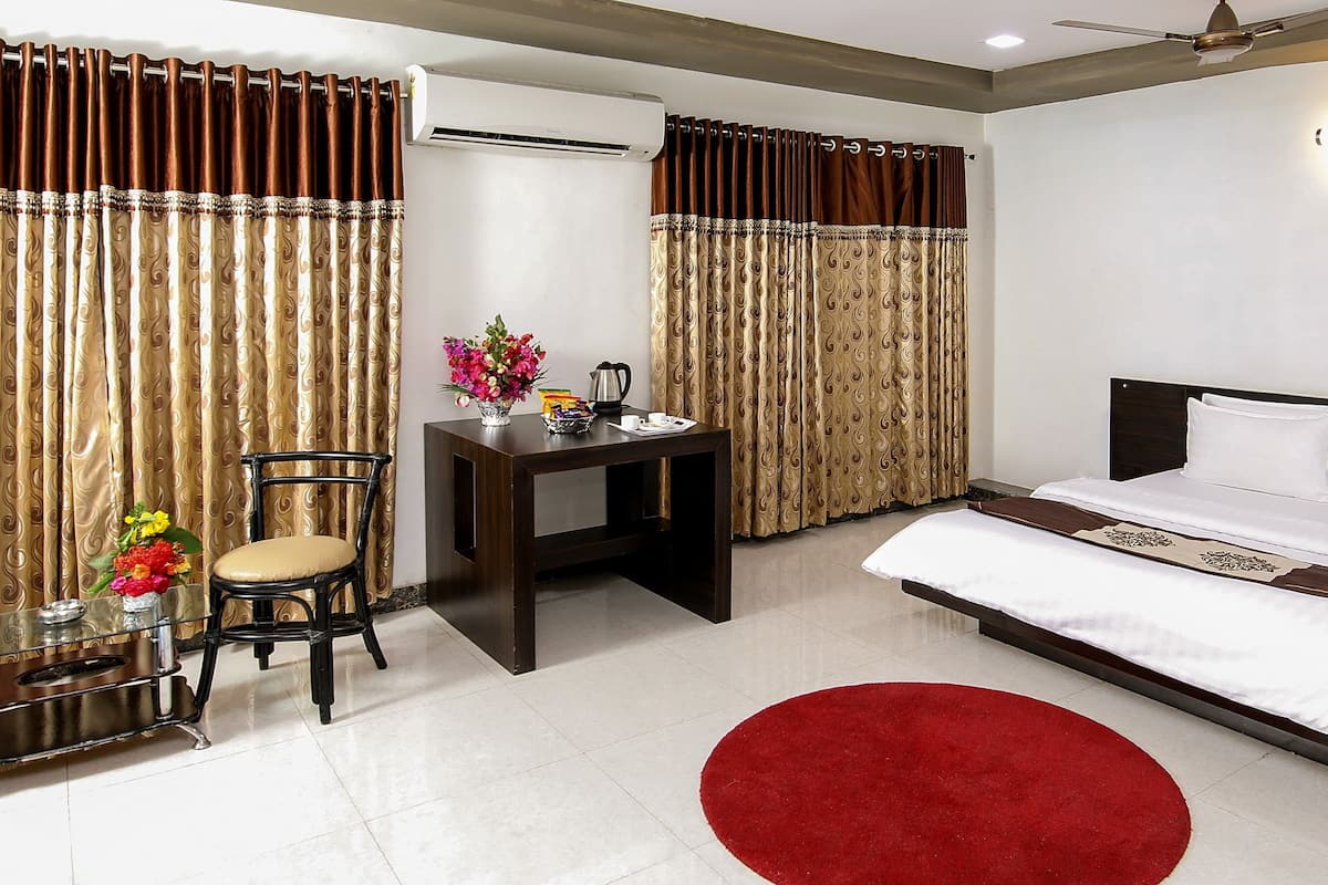 A hotel room with a bed, a desk, a chair, and a red rug.