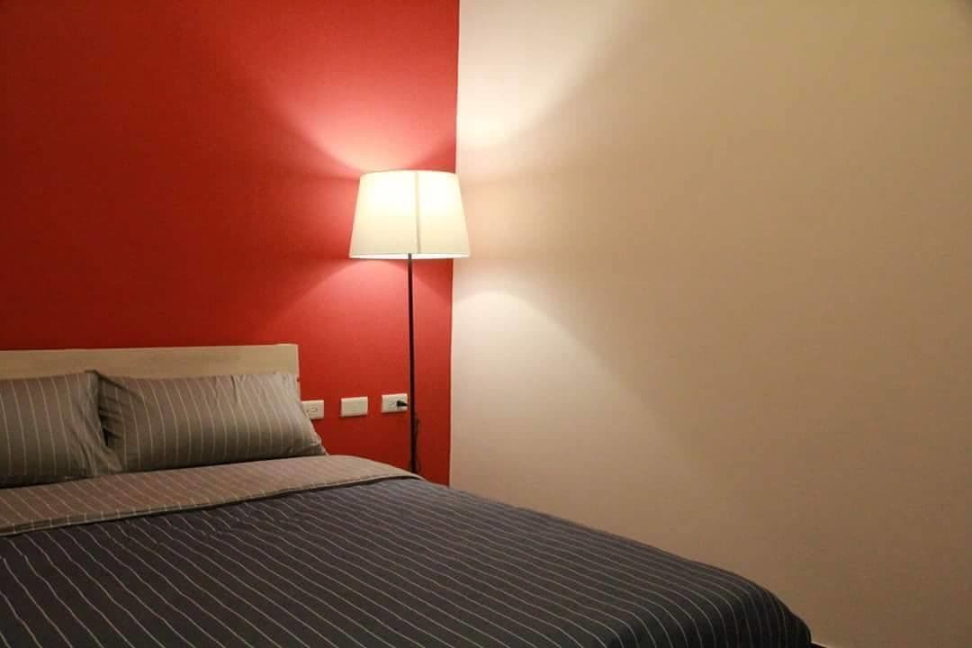 A bed with striped bedding, a red wall, and a floor lamp.