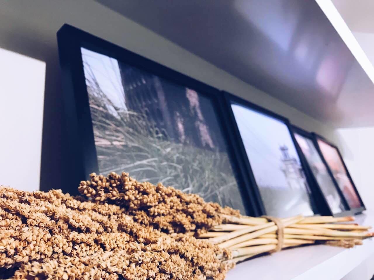 A wall-mounted display with framed pictures and a bunch of dried flowers in the foreground.
