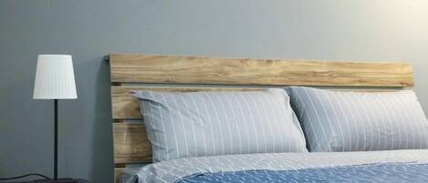 Un dormitorio con cabecera de madera, una cama con ropa de cama a rayas y una mesita de noche con lámpara.