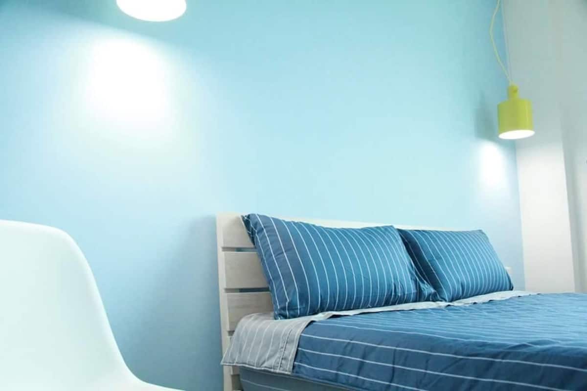 A bedroom with a bed, a chair, and a hanging light fixture.