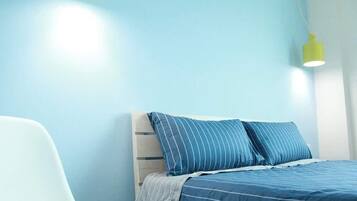 A bedroom with a bed, a chair, and a hanging light fixture.
