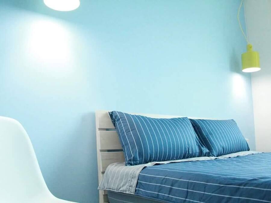 A bedroom with a bed, a chair, and a hanging light fixture.