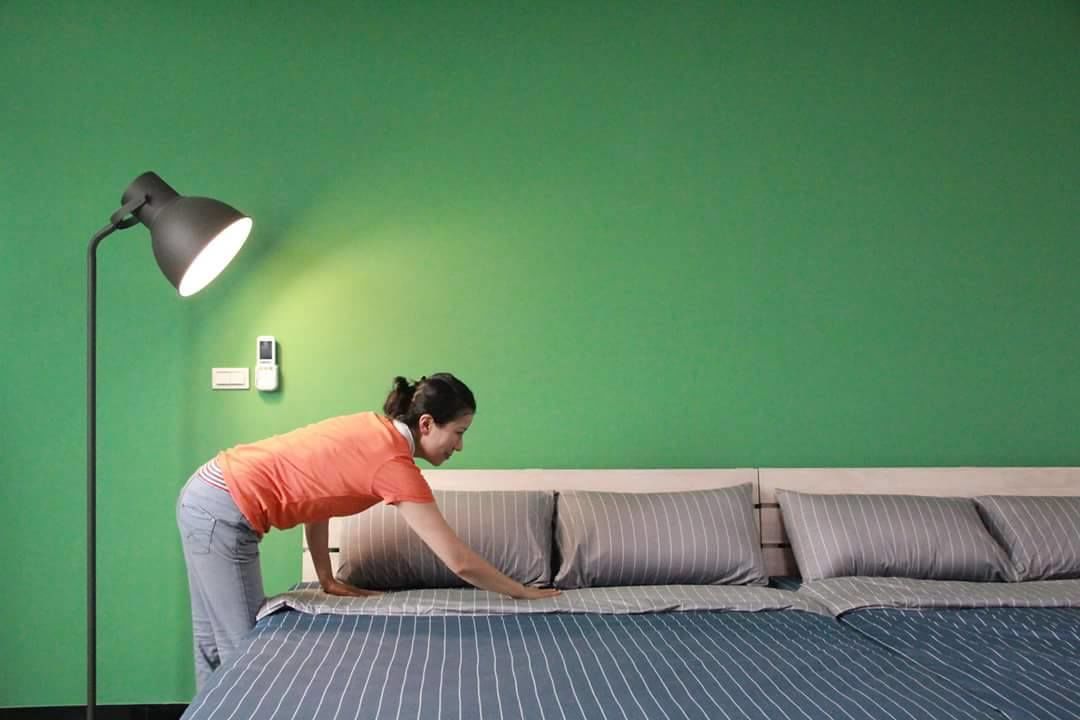 A person adjusting a bed in a room with green walls and a black floor lamp.