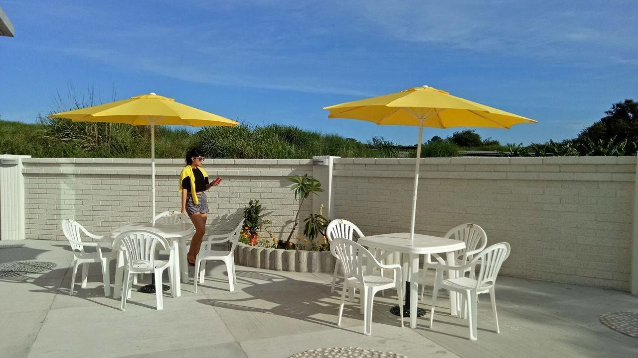 An outdoor patio area with white plastic chairs and tables, two yellow umbrellas, and a brick wall in the background.