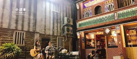 An outdoor courtyard with a stage for live music, surrounded by buildings with traditional architecture and a small garden area.
