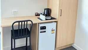 Una kitchenette compacta con microondas, un refrigerador pequeño y cafetera sobre una encimera de madera.