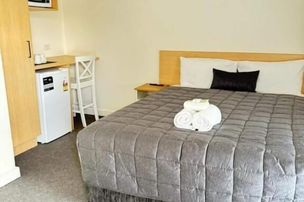 A hotel room with a large bed, a small desk, a microwave, and a refrigerator.