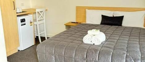 Ein Hotelzimmer mit einem großen Bett, einem kleinen Schreibtisch, einer Mikrowelle und einem Kühlschrank.