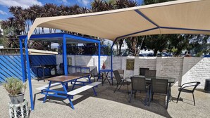 Un patio al aire libre con asientos azules y beige, un muro de ladrillo blanco y una zona con sombra.